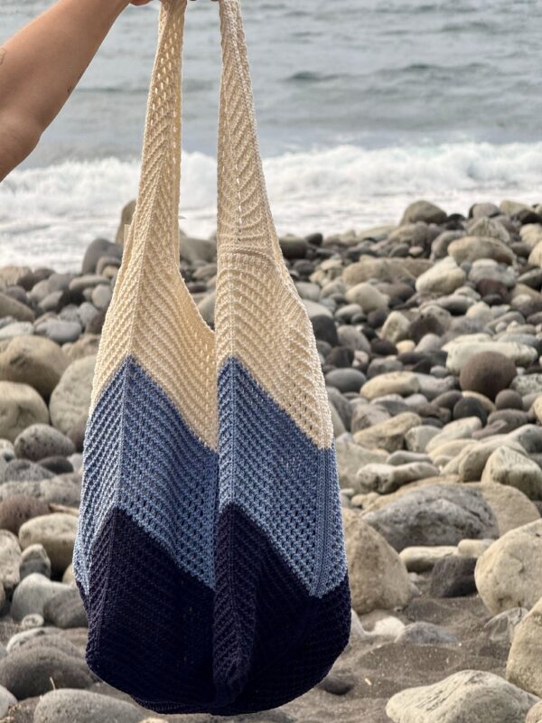 Bolso saco de crochet artesanal en tonos azules y blanco en una playa de Canarias